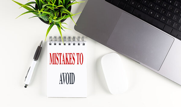 MISTAKES TO AVOID text on a notebook with laptop, mouse and pen .