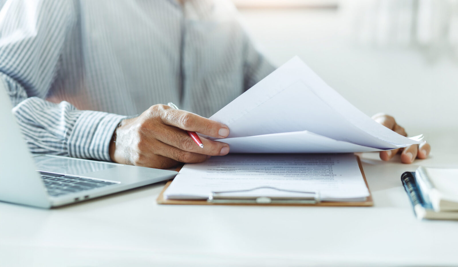 Asian businessman reviewing document reports at office workplace with computer laptop. legal expert, professional lawyer reading and checking financial documents or insurance contract, close-up shot